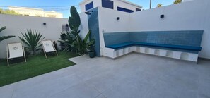 Un espace patio avec un banc bleu, un petit jardin avec des plantes vertes et un mur blanc avec une fenêtre.