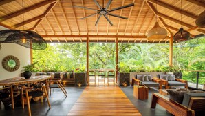 A spacious indoor area with a wooden floor, seating arrangements, and a view of lush greenery outside. - Luxurious Beachfront Villa with Private Pool in Punta Uva (Punta Uva)