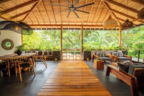 A spacious indoor area with a wooden floor, seating arrangements, and a view of lush greenery outside. - Luxurious Beachfront Villa with Private Pool in Punta Uva (Punta Uva)