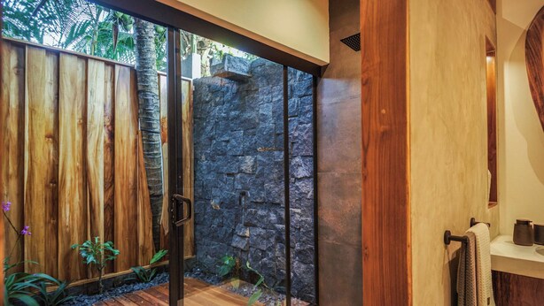 A modern bathroom with a glass shower enclosure, wooden accents, and a stone wall. - Luxurious Beachfront Villa with Private Pool in Punta Uva (Punta Uva)