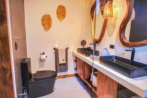 A modern bathroom with a black toilet, a wooden vanity with a large mirror, and a black sink. - Luxurious Beachfront Villa with Private Pool in Punta Uva (Punta Uva)