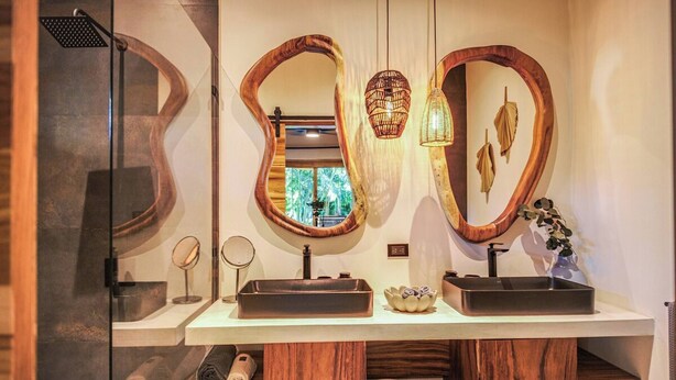 A bathroom with two sinks, a shower, and a mirror with a unique curved design. - Luxurious Beachfront Villa with Private Pool in Punta Uva (Punta Uva)