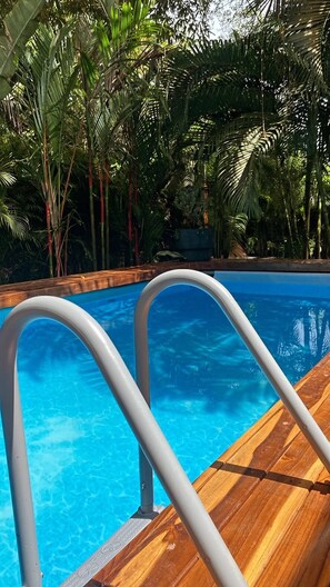 Piscina de color blau clar amb terrassa de fusta i barana metàl·lica al costat.