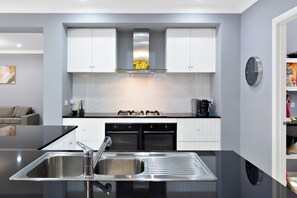 Une cuisine moderne avec des meubles blancs, un évier en acier inoxydable et une cuisinière à gaz.