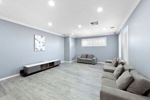 Une pièce spacieuse avec un canapé gris, une petite banquette grise, une console blanche et un tableau accroché au mur.