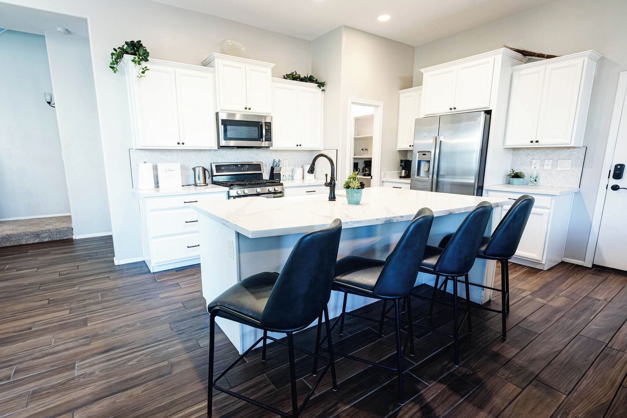A modern kitchen with white cabinets, a central island with bar stools, stainless steel appliances, and a herringbone wood floor.