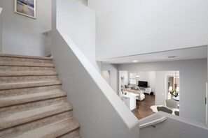 A staircase leading to a living area with a flat-screen TV, sofa, and dining table. - Casa Encanto  - EV Charger, Pool, AC, H20 Filter (Goodyear)