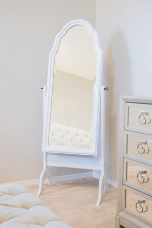 A white vanity with a mirror, a tufted white chair, and a dresser with drawers. - Casa Encanto  - EV Charger, Pool, AC, H20 Filter (Goodyear)
