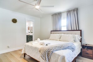 Ein Schlafzimmer mit einem Bett, einem Deckenventilator, einem Fenster mit Vorhängen und einem Holznachttisch.