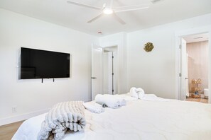 A bedroom with a bed, a flat-screen TV mounted on the wall, a ceiling fan, and a door leading to another room. - Fully Remodeled Brandon Escape w/ Fenced Yard! (Brandon)
