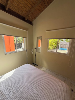 A room with a bed, two windows with orange curtains, a ceiling fan, and a view of a pool and greenery outside. - Luxurious 5-Bedroom House with Private Pool in Cabrera (Cabrera)