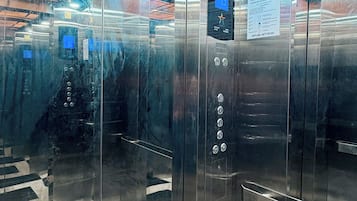 L’intérieur d’un ascenseur, avec des portes en verre réfléchissant, un panneau de commande doté de boutons et un écran numérique.