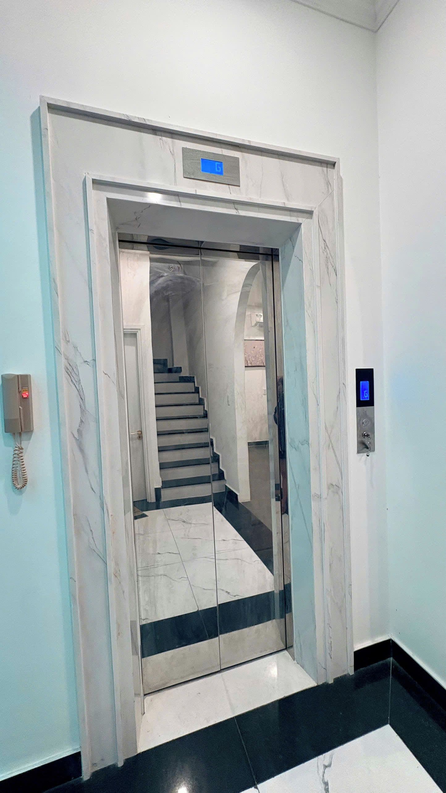 Een lift met een marmeren afwerking en een digitaal display dat de verdieping aangeeft.