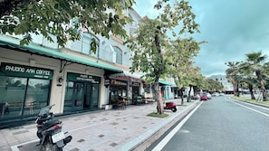 Rua com cafés e restaurantes, uma scooter estacionada na calçada e uma avenida arborizada.