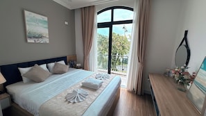 Habitación de hotel con una cama grande, vistas al exterior y una mesita con un jarrón de flores.
