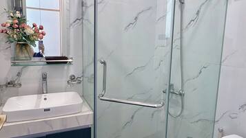 A bathroom with a glass-enclosed shower, a sink, a toilet, and a mirror with a vase of flowers.