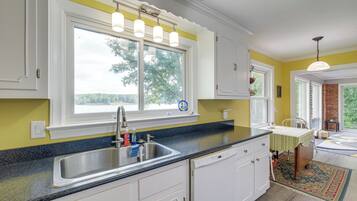 A kitchen with a large window, stainless steel sink, and white cabinetry.