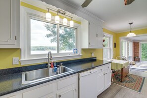 A kitchen with a large window, stainless steel sink, and white cabinetry.