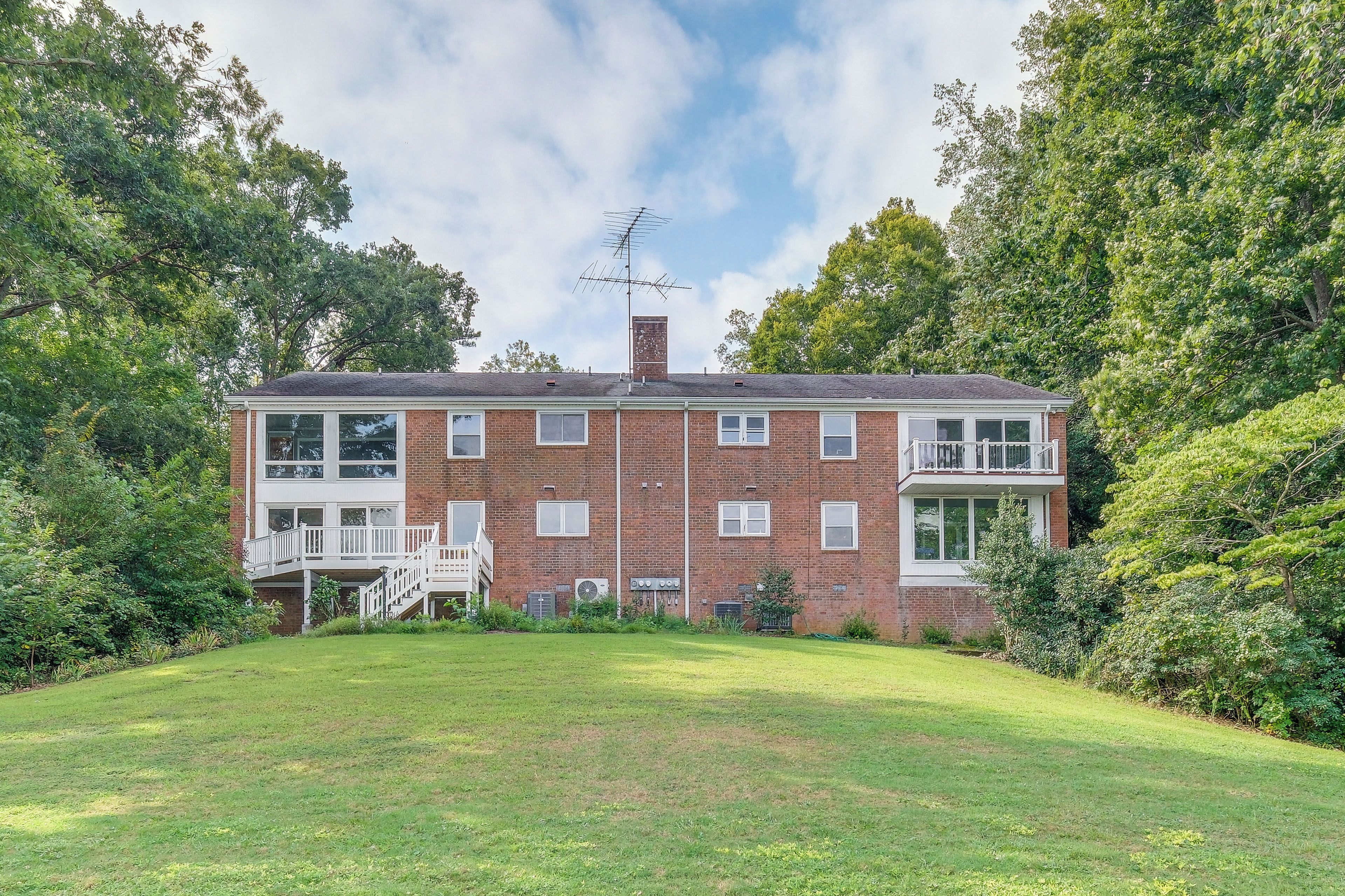 A two-story brick building with a balcony on the second floor, surrounded by greenery.