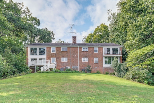 A two-story brick building with a balcony on the second floor, surrounded by greenery.