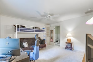 A room with a bunk bed, a desk with a computer, a chair, a lamp, and a ceiling fan.