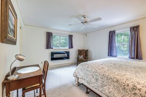 A bedroom with a bed, a desk with a chair, a ceiling fan, and two windows with curtains.