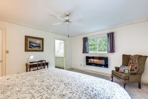 A bedroom with a bed, a desk, a chair, a ceiling fan, a window with curtains, and a painting on the wall.