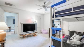 Une chambre avec un lit superposé, une télévision, un bureau avec un ordinateur et un ventilateur de plafond.