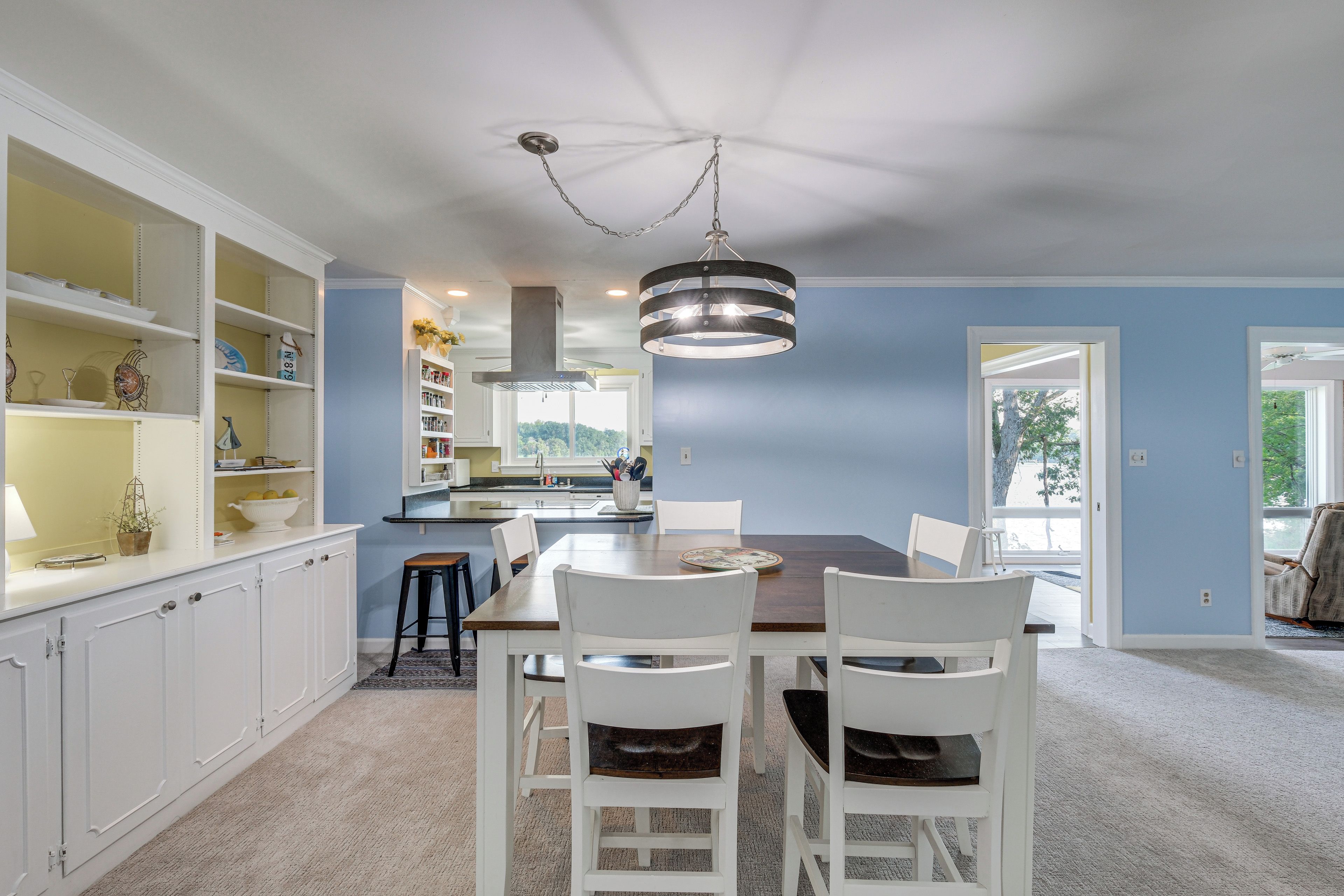 Un coin repas avec une table et des chaises, une cuisine en arrière-plan et une vue par la fenêtre.