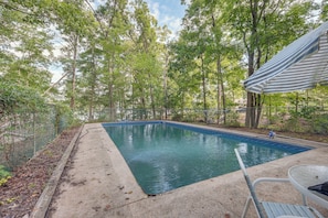 A swimming pool with a metal fence, surrounded by trees and a covered patio area.