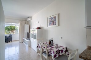 A dining area with a table set for two, a television, and a window with curtains. - Studio in Nerja With Sea Views & Pool (Nerja)
