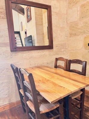 Een houten eettafel met vier stoelen, geplaatst tegen een structuurrijke muur met een spiegel erboven.