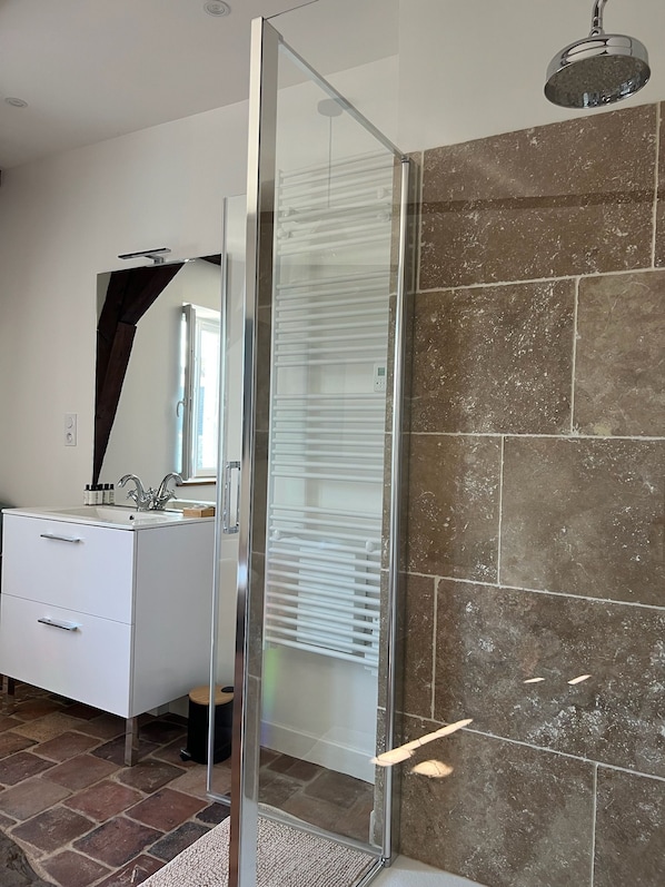 Un baño moderno con mampara de vidrio, tocador blanco y un espejo grande.