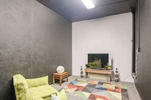 Una habitación con una televisión sobre un soporte de madera, una alfombra estampada y un sofá verde.