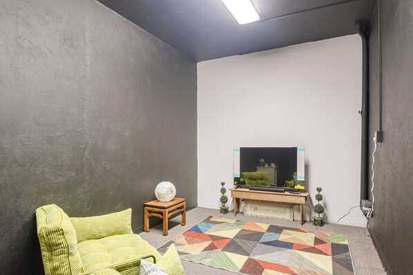 A room with a television on a wooden stand, a patterned rug, and a green sofa. - On Main St! Walkable Family Apartment in Princeton (Princeton)