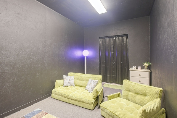 A room with a sofa, two armchairs, a floor lamp, a dresser, and a window with curtains.