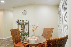 A dining area with a round glass table, wicker chairs, a wall clock, and a shelf with decorative items. - On Main St! Walkable Family Apartment in Princeton (Princeton)