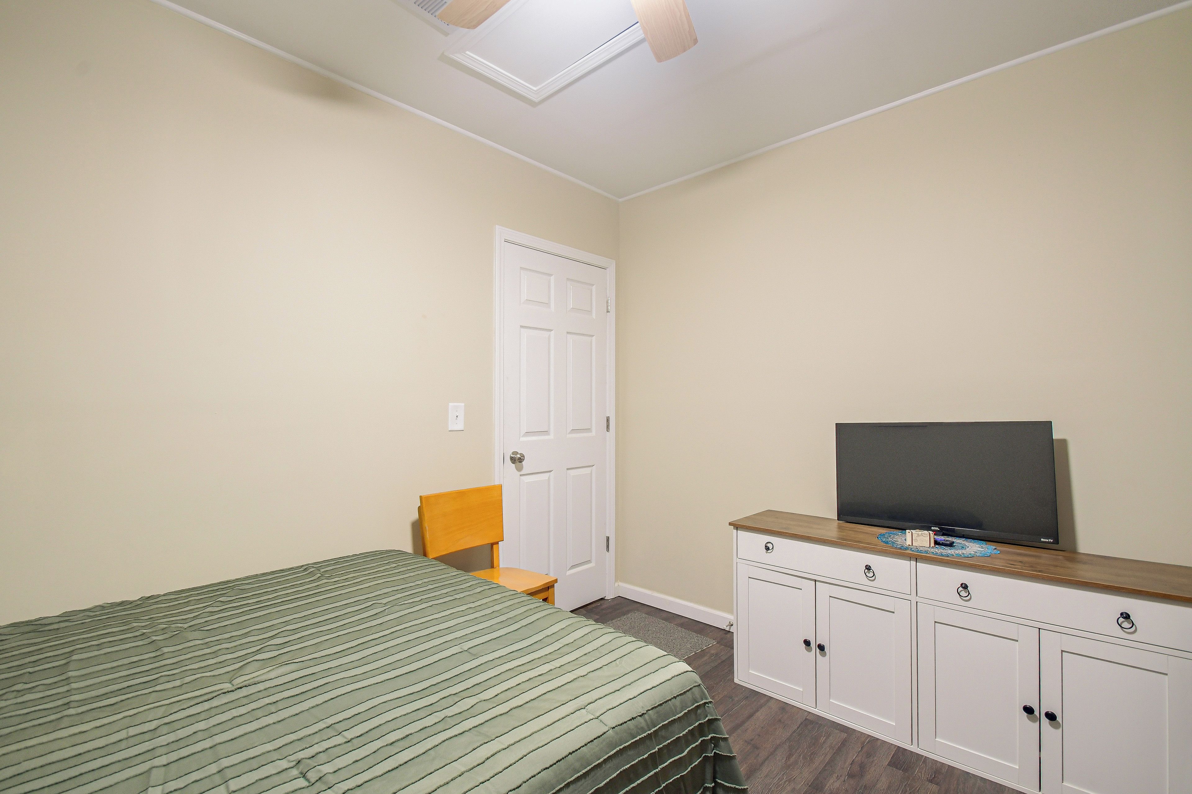 A bedroom with a bed, a chair, a television on a cabinet, and a door.