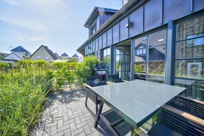 Une terrasse extérieure moderne, dotée d’une table en verre, d’un barbecue et offrant une vue sur les maisons voisines.