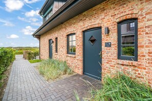 Ein Backsteinhaus mit einer dunklen Tür, Fenstern und einem gepflasterten Weg.