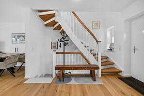 Eine Treppe mit Holzbodenstufen und weißen Geländern, ein Essbereich mit Tisch und Stühlen sowie ein Kleiderständer.
