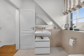Une salle de bain moderne avec un lavabo blanc, des toilettes et un espace douche.