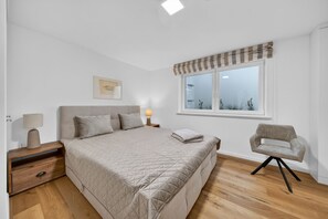 Une chambre à coucher comprenant un lit, des tables de chevet, une chaise, une fenêtre et une lampe fixée au mur.