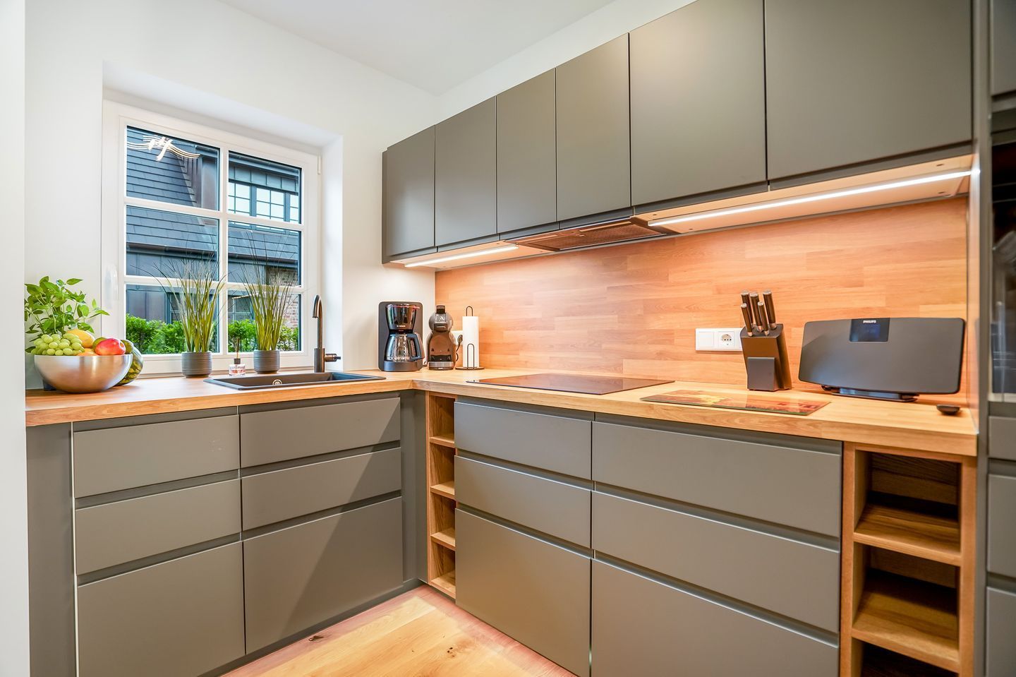 A modern kitchen with grey cabinets, a wooden countertop, and a built-in stove.