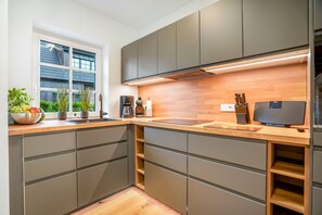 A modern kitchen with grey cabinets, a wooden countertop, and a built-in stove. - Beachfront accommodation for 5 people in a new building with a terrace and private sauna - (Hörnum (Sylt))