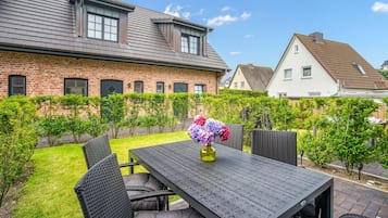 A patio with a table and chairs, surrounded by a brick building and a hedge.