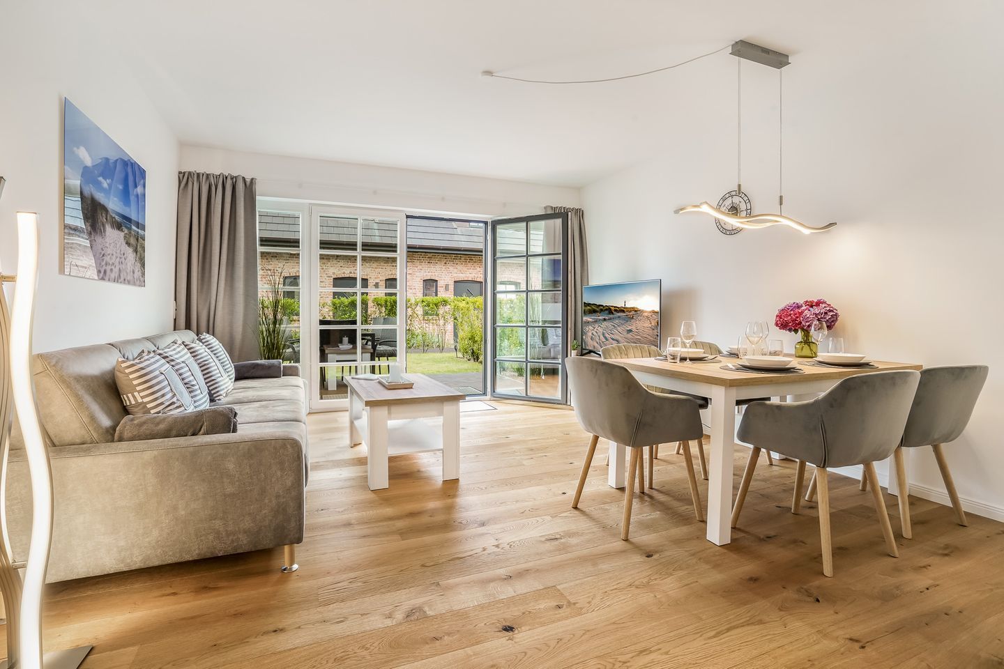 Een moderne woonkamer met een bank, een eettafel met stoelen en een grote schuifpui die uitkomt op een tuin.