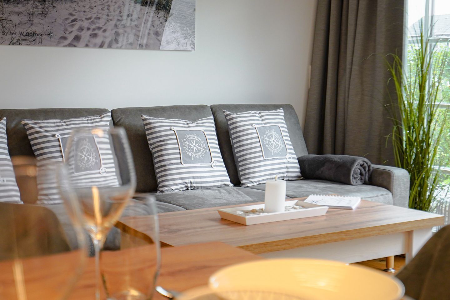A modern living room with a grey sofa, striped pillows, a wooden coffee table, and a large window with curtains.