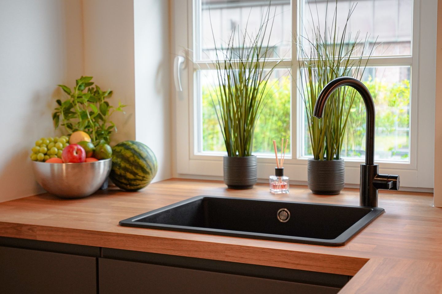 A kitchen with a black sink, a bowl of fruit, and two potted plants.