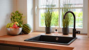 A kitchen with a black sink, a bowl of fruit, and two potted plants.